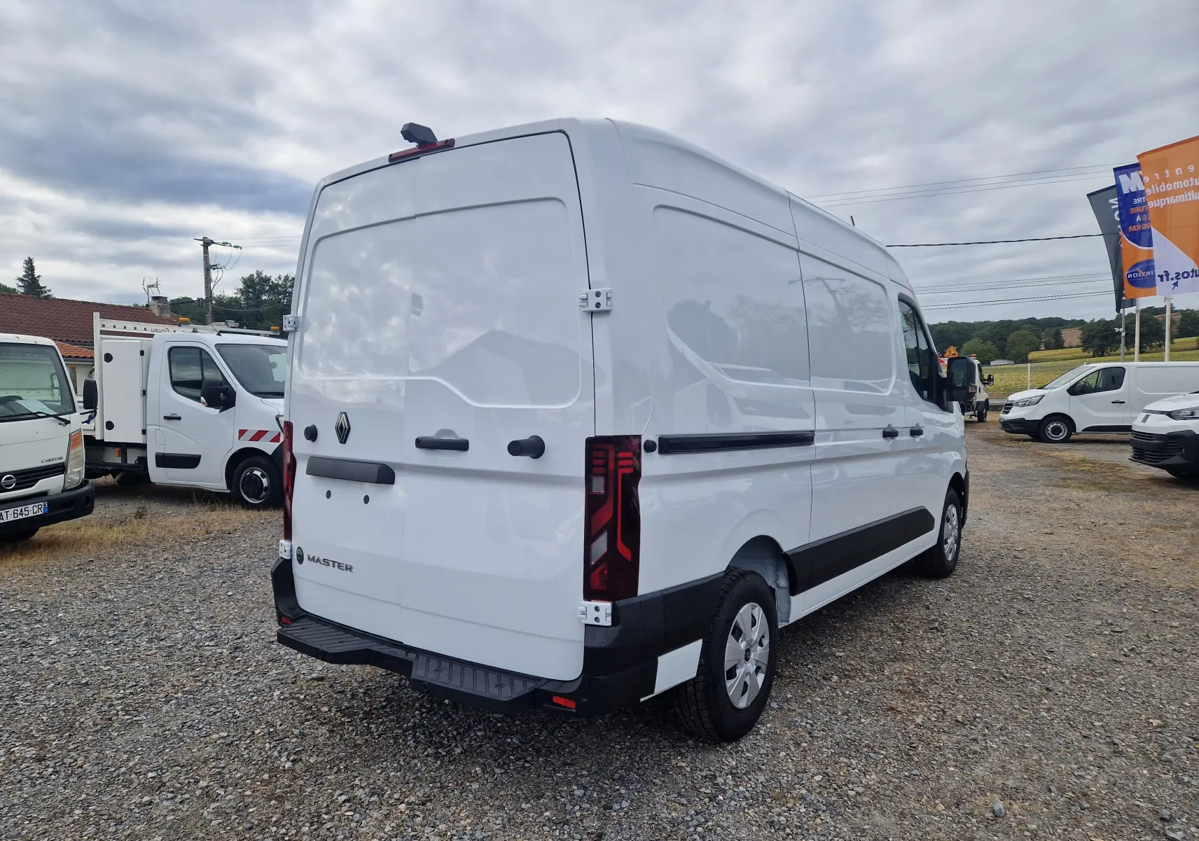 Vue 3/4 arrière droite d’un utilitaire Renault Master blanc, avec feux arrière LED et porte arrière fermée sur un sol gravillonné.