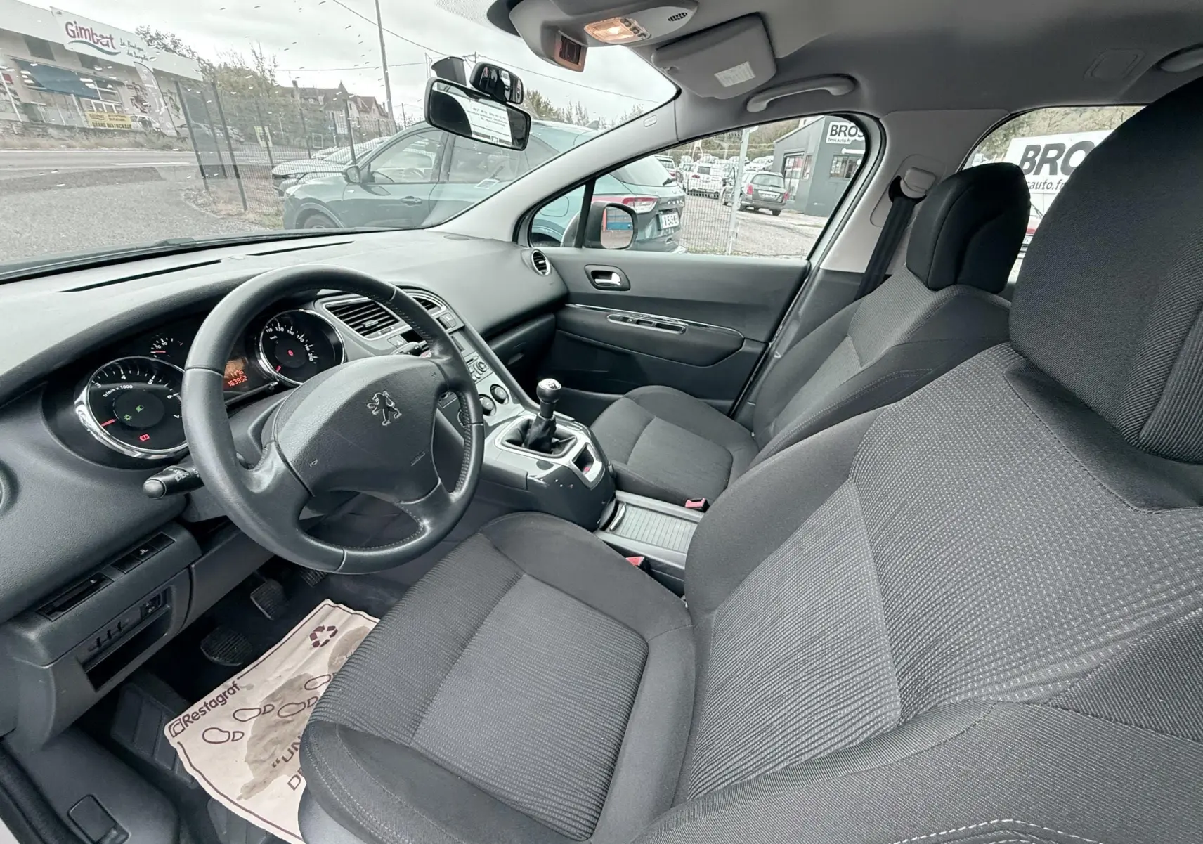 Intérieur avant du Peugeot 5008 2010 en tissu gris, vue côté conducteur avec volant et levier de vitesses manuel visibles.