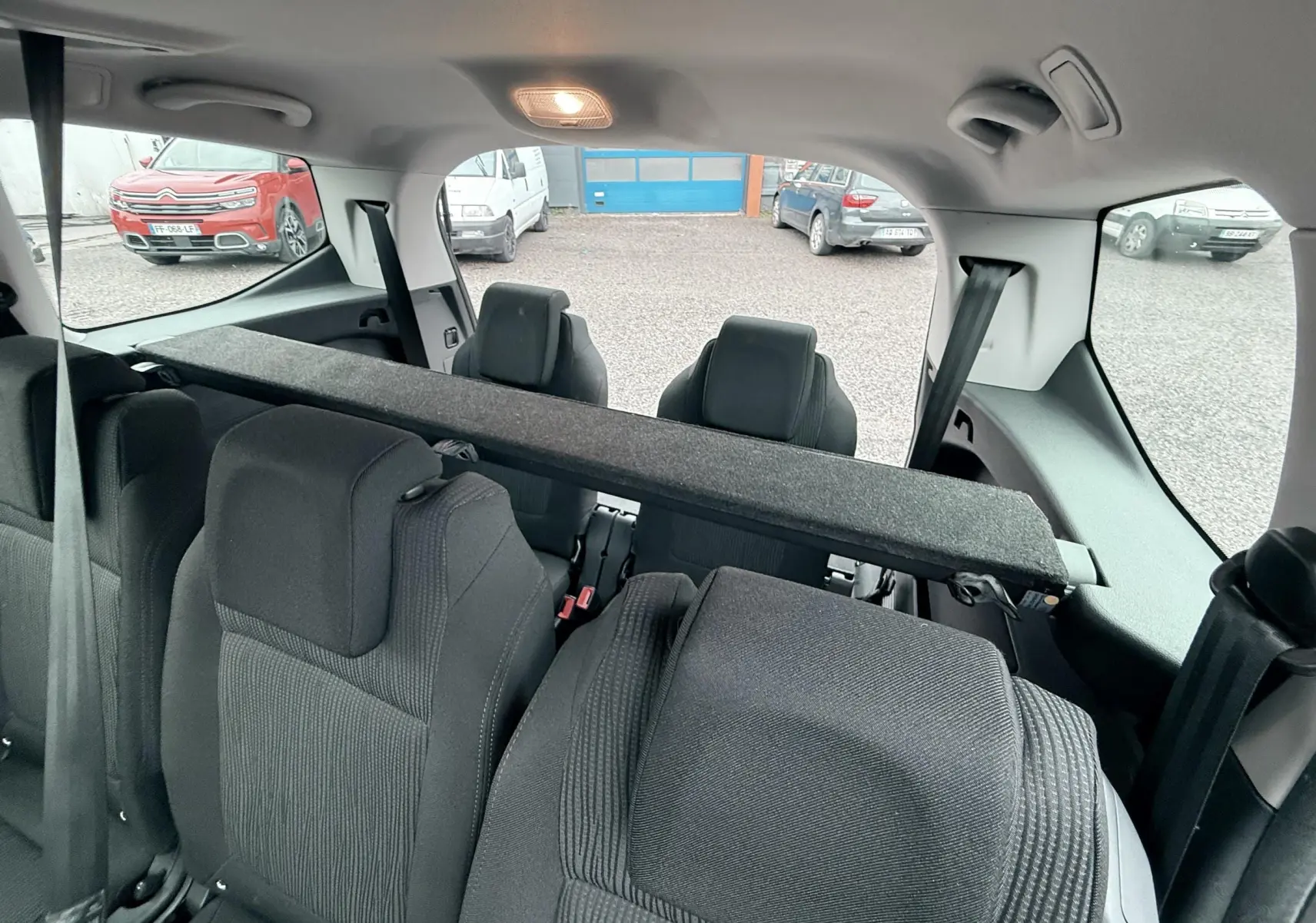 Vue intérieure arrière du Peugeot 5008 gris de 2010, montrant les sièges arrière en tissu et la plage arrière partiellement relevée.
