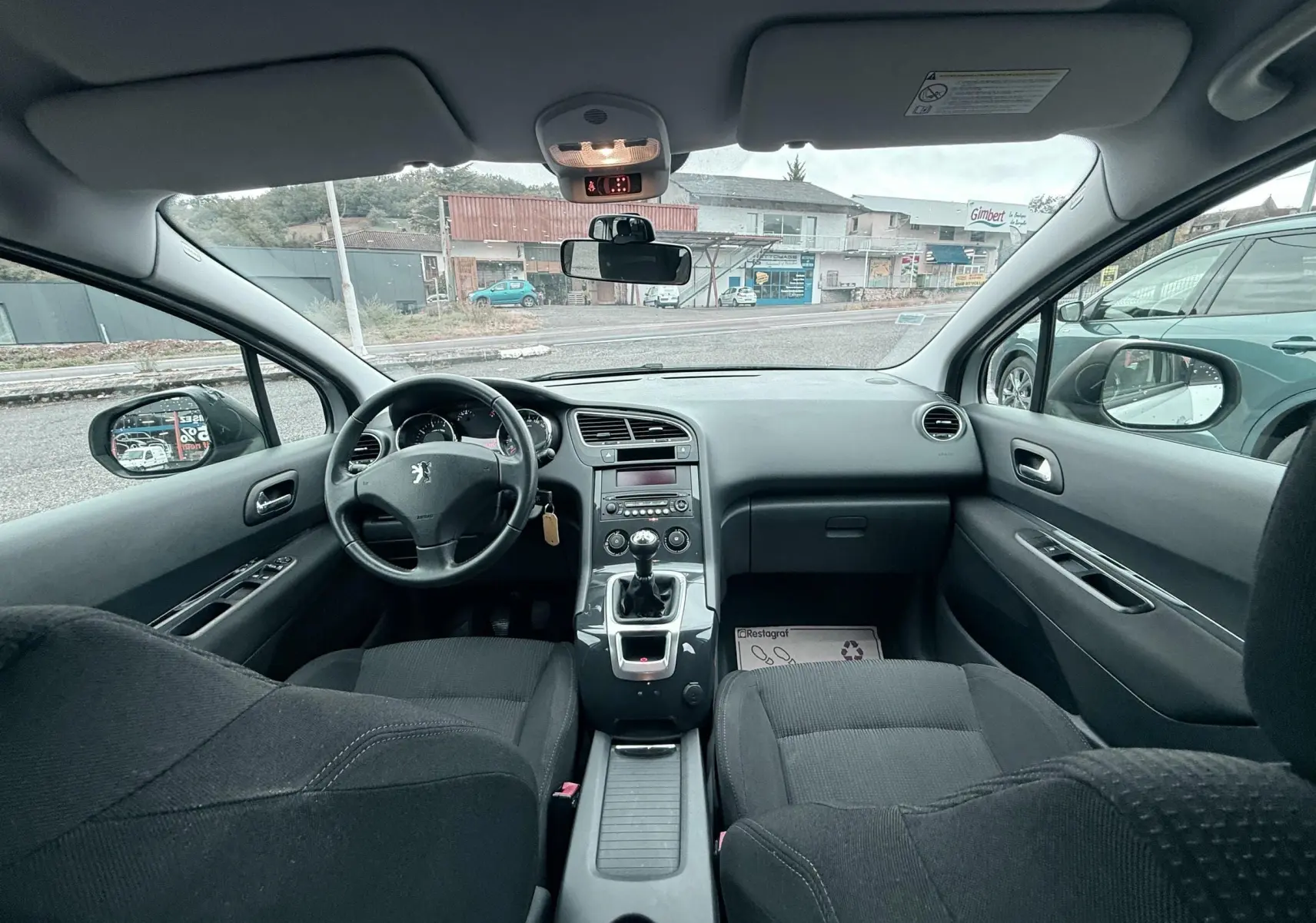 Vue intérieure avant du Peugeot 5008 gris de 2010, montrant le tableau de bord, volant et levier de vitesses manuel.