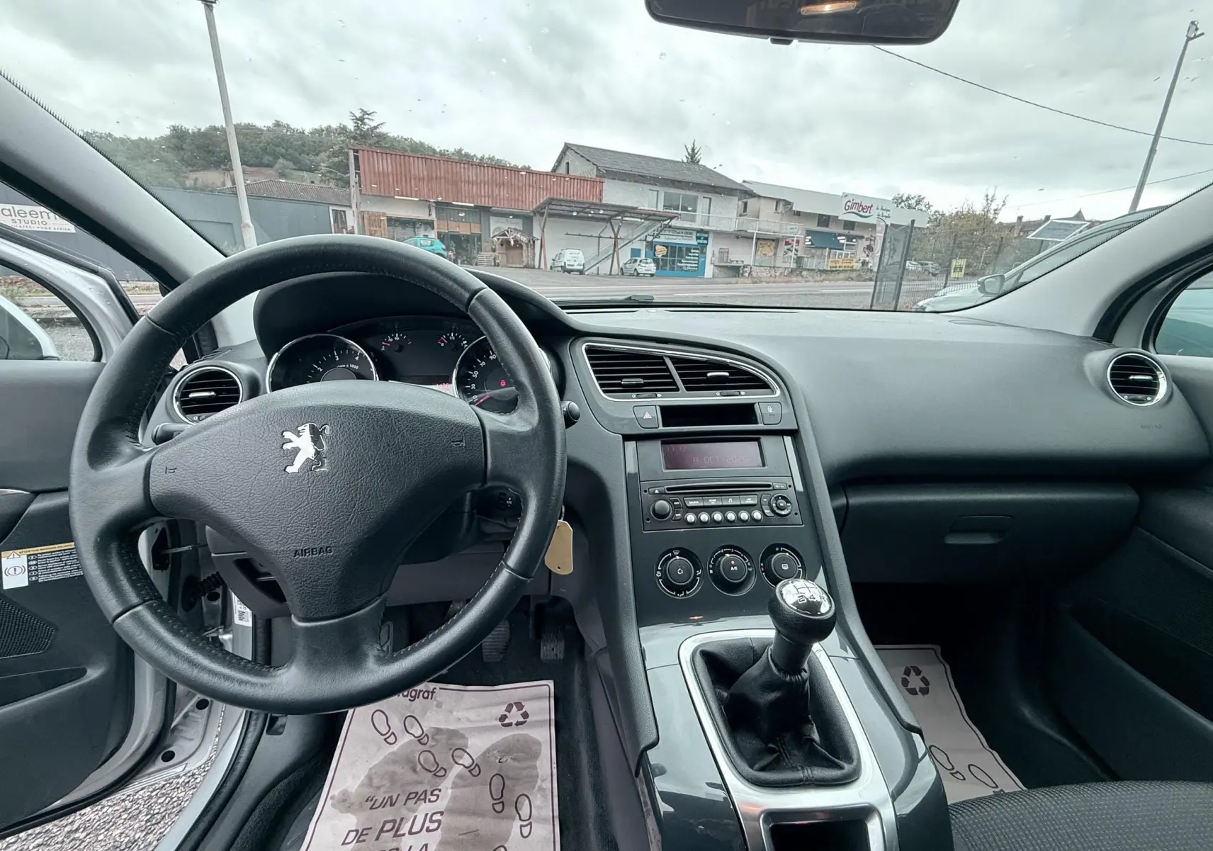 Vue intérieure du tableau de bord et volant en cuir noir d'une Peugeot 5008 2010 avec boîte manuelle, ambiance sobre et fonctionnelle.