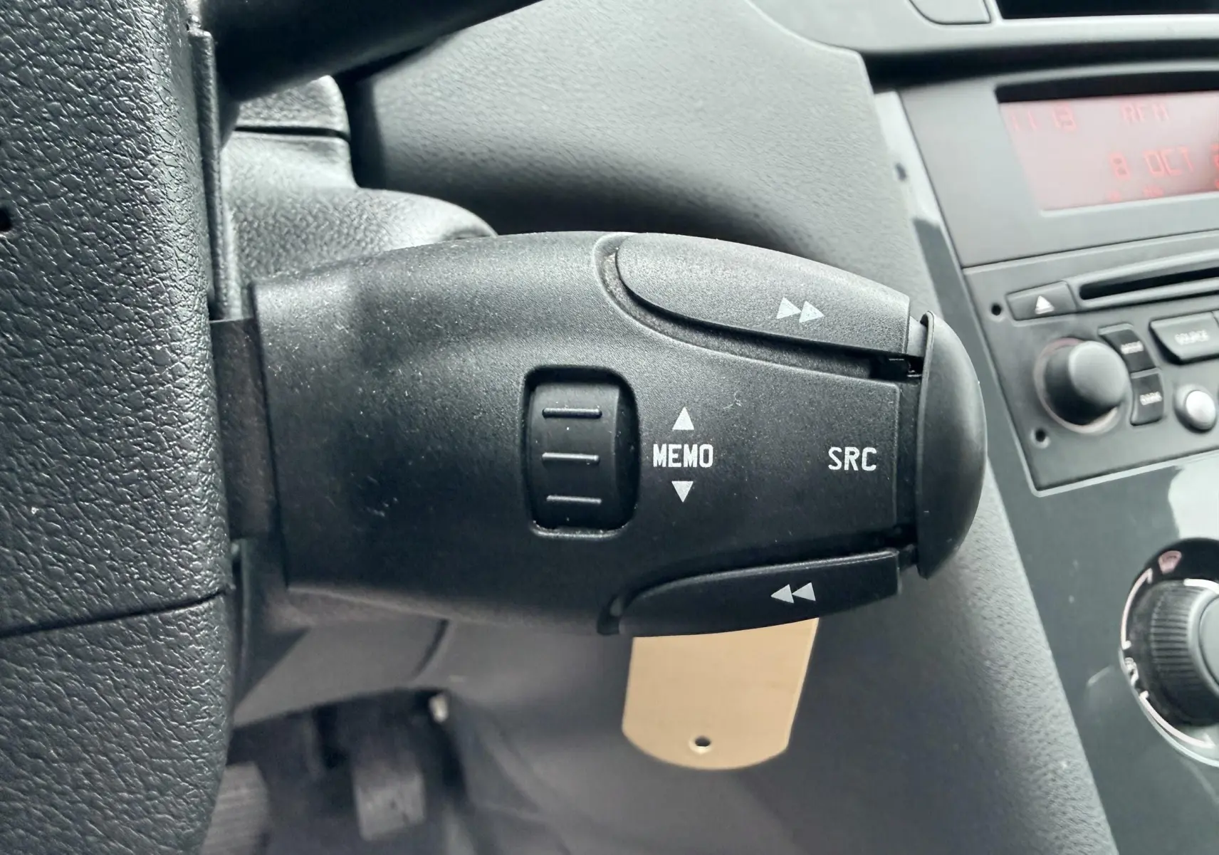 Gros plan sur la commande au volant gauche du Peugeot 5008 gris, avec boutons MEMO et SRC visibles.