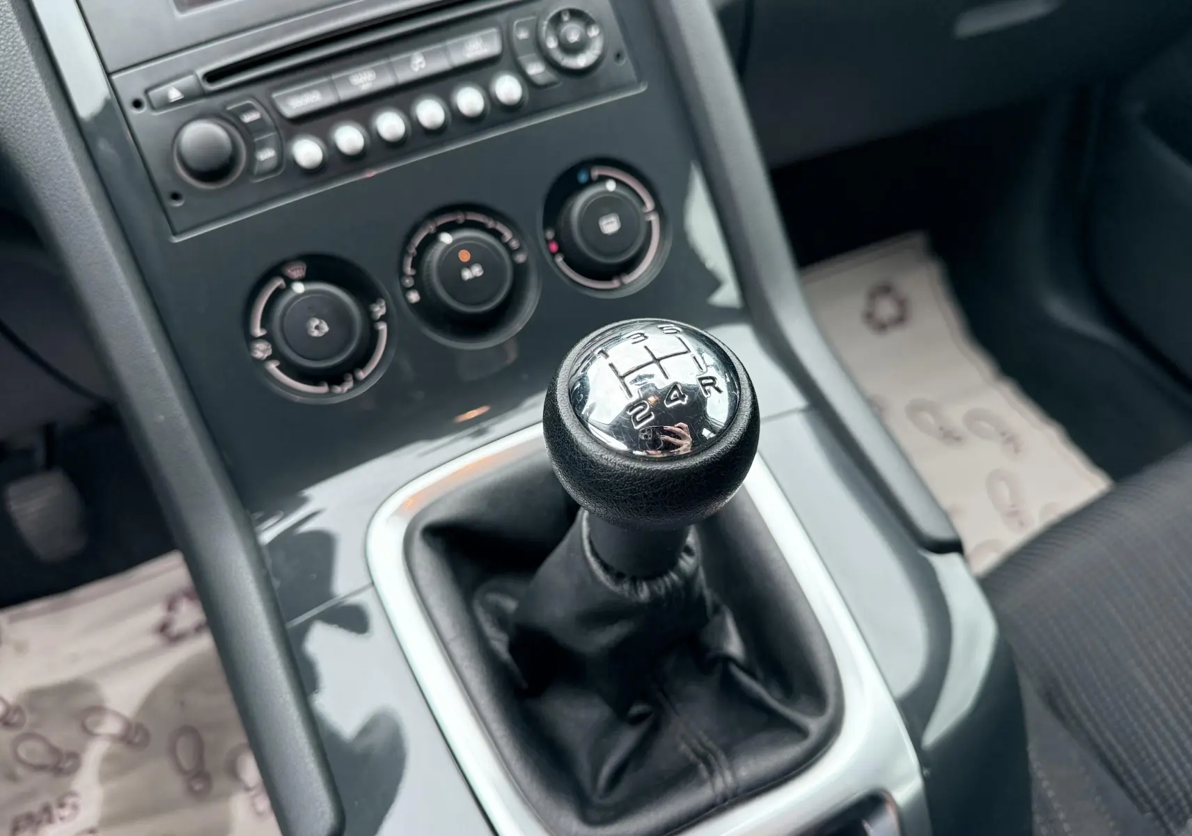 Gros plan sur le levier de vitesses manuel noir et chrome dans l’habitacle gris du Peugeot 5008, avec commandes de climatisation visibles.