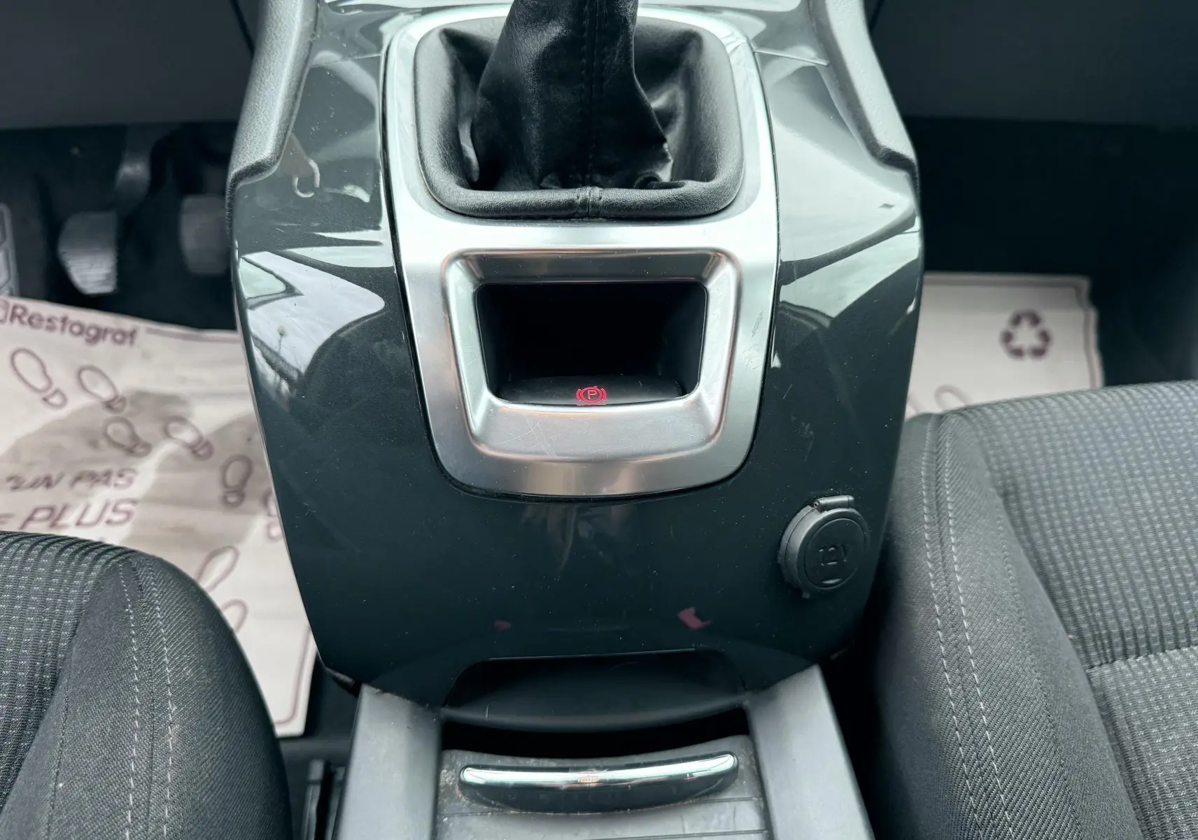 Vue rapprochée de la console centrale grise du Peugeot 5008 2010 avec levier de vitesse manuel et prise 12V visible entre les sièges en tissu gris.