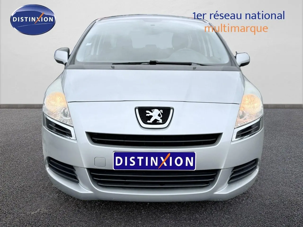 Vue frontale d'un Peugeot 5008 gris avec phares allumés sur fond neutre.