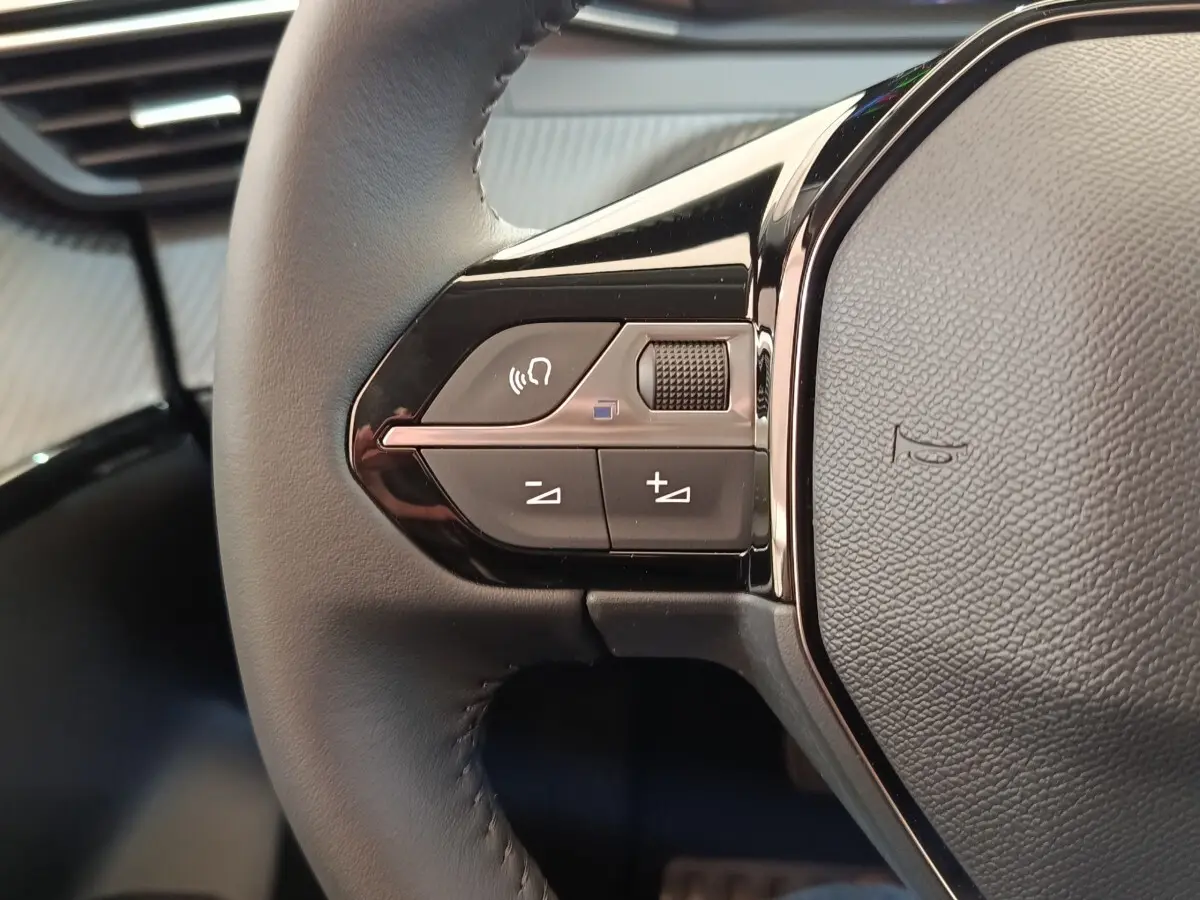 Gros plan sur les commandes gauche du volant cuir noir du Peugeot 208 électrique blanc, avec boutons multifonctions.
