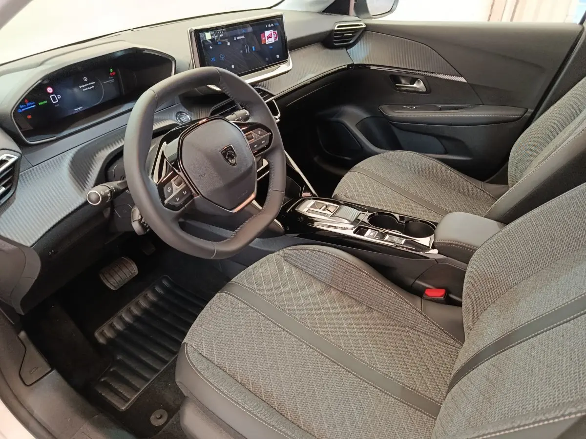 Vue intérieure avant droite de la Peugeot 208 électrique 2024 avec sièges gris et tableau de bord numérique.