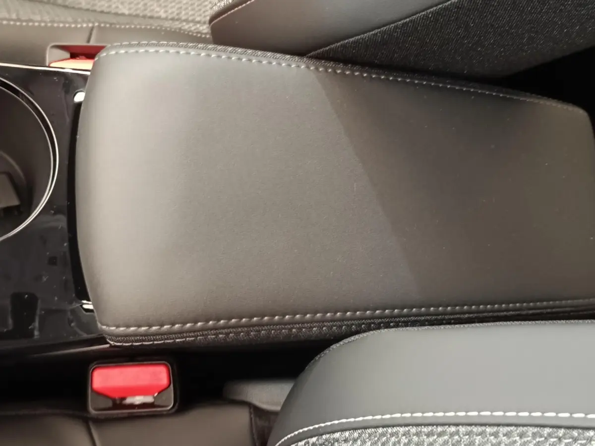 Détail de l'accoudoir central en cuir noir avec surpiqûres blanches dans l'habitacle d'une Peugeot 208 électrique.