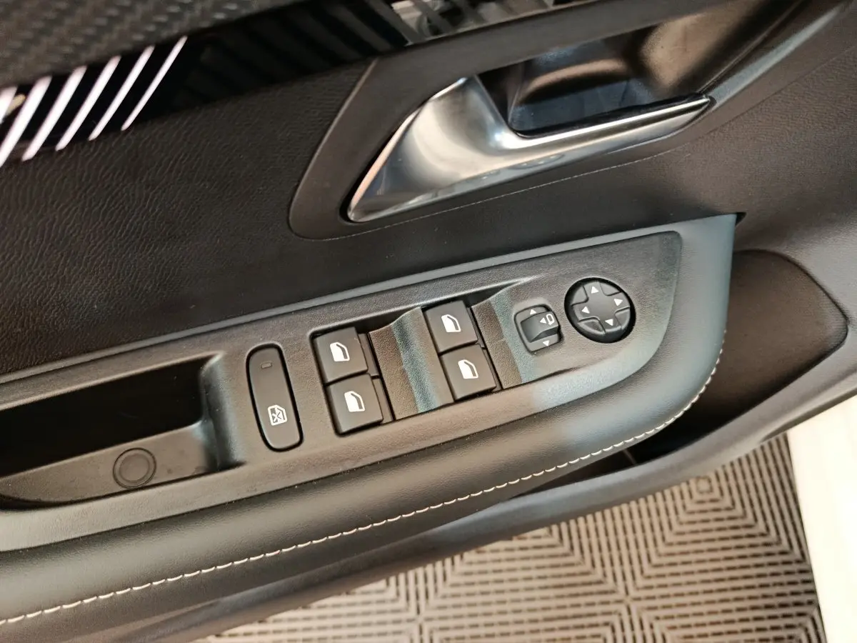 Gros plan sur la commande des vitres électriques et réglage des rétroviseurs côté conducteur de la Peugeot 208 blanche 2024.