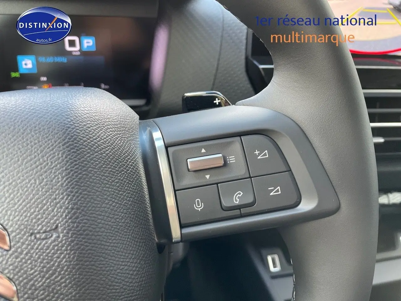 Gros plan sur les commandes au volant à droite de la Citroën C4 2024, finition gris platinium métal, avec affichage numérique en arrière-plan.