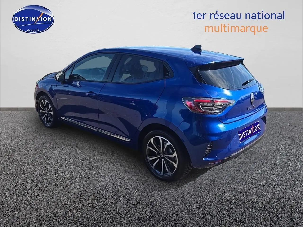 Renault Clio V bleu iron en 3/4 arrière droit, avec jantes alu et becquet arrière distinctif.