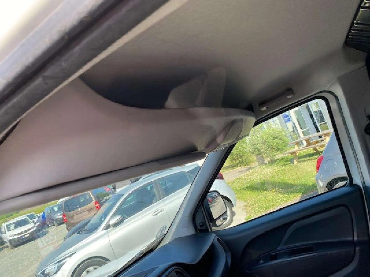 Vue intérieure côté conducteur du Fiat Doblo blanc 2017, montrant le tableau de bord et la portière avec vitre baissée.