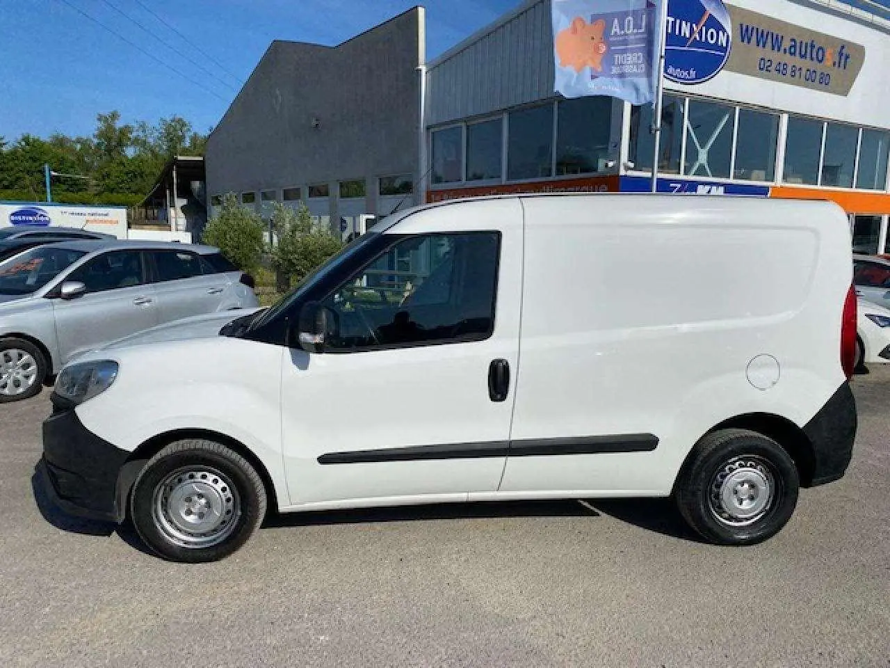 Vue de profil côté gauche d'un utilitaire FIAT Doblo blanc avec porte latérale droite et pare-chocs noirs non peints.