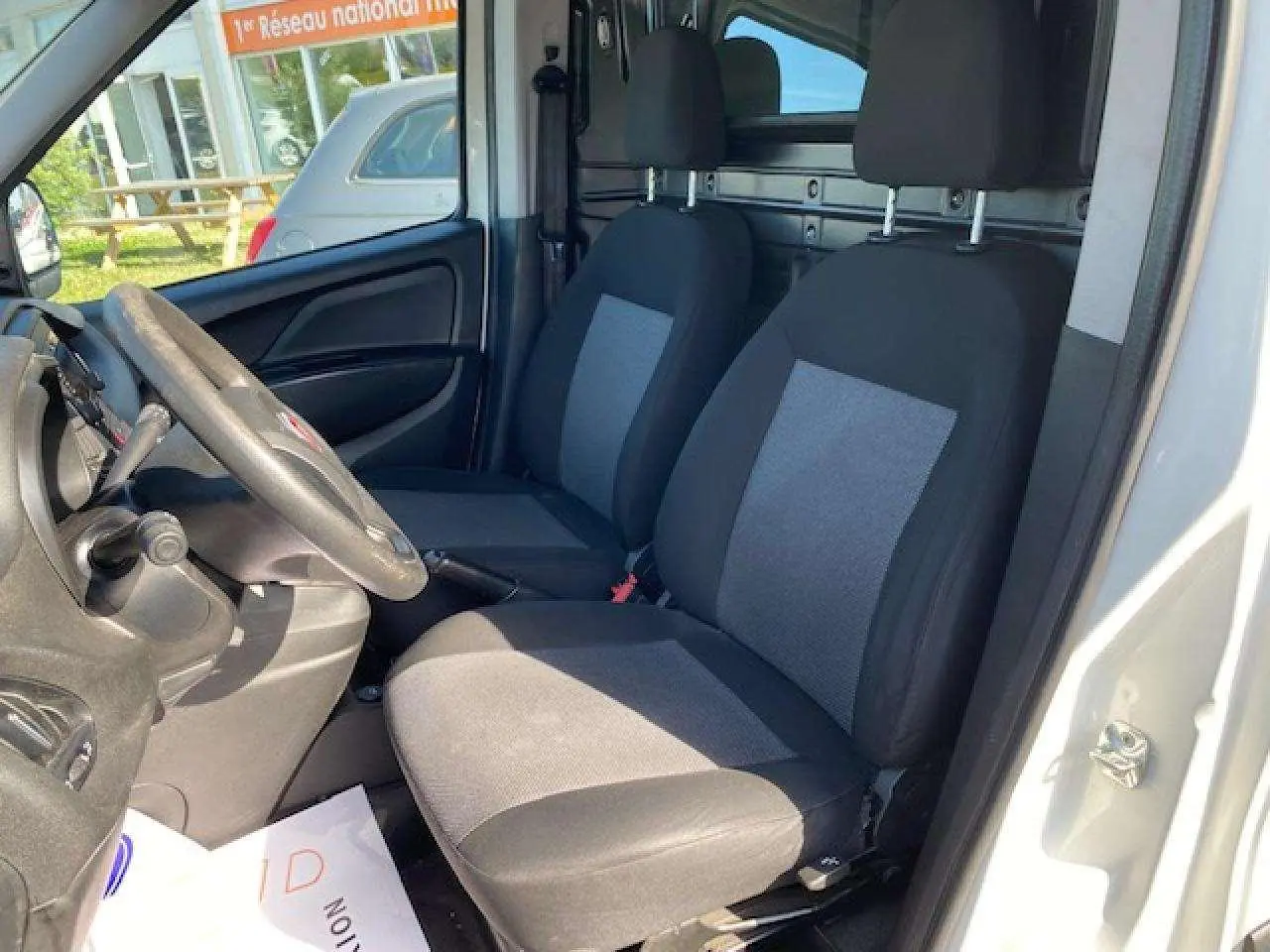 Vue intérieure côté conducteur du Fiat Doblo blanc 2017 montrant les sièges avant et la paroi vitrée de séparation.