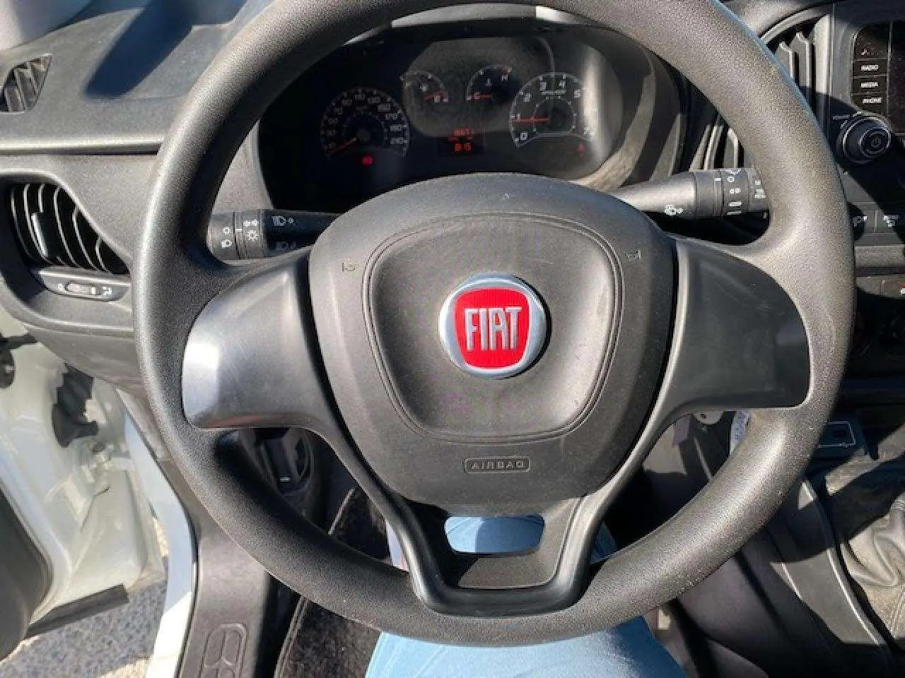 Vue rapprochée du volant noir avec logo FIAT rouge dans l'habitacle d'un Fiat Doblo blanc de 2017.