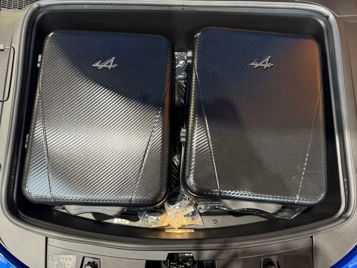 Vue plongeante sur le coffre avant bleu d'une Alpine A110 Legende 2019 avec deux valises carbone marquées du logo Alpine.
