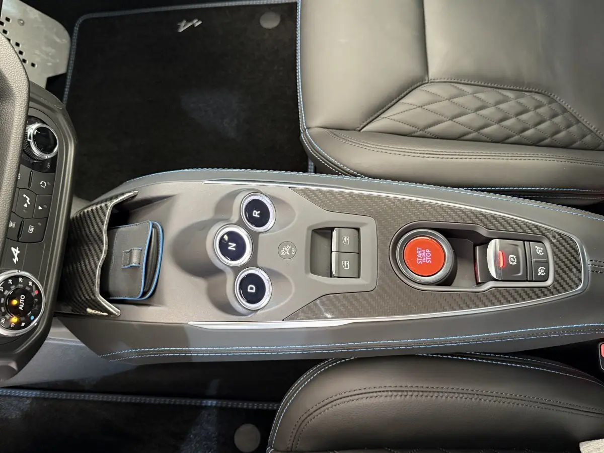 Vue plongeante sur la console centrale en carbone de l'Alpine A110 Legende 2019 avec bouton start/stop rouge et cuir gris.