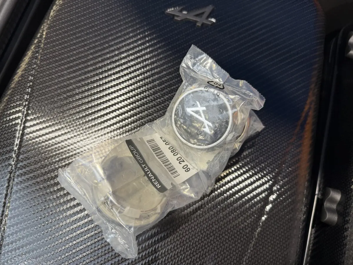 Gros plan sur un badge Alpine A110 emballé posé sur une surface en fibre de carbone à l'intérieur du véhicule.