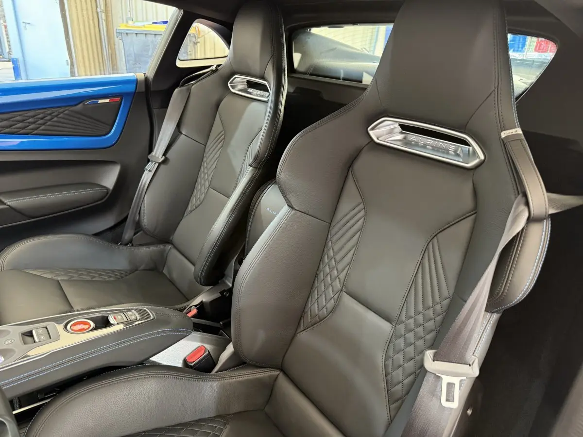 Vue intérieure rapprochée des sièges en cuir noirs de l'Alpine A110 Legende avec détails bleus sur la portière bleue.