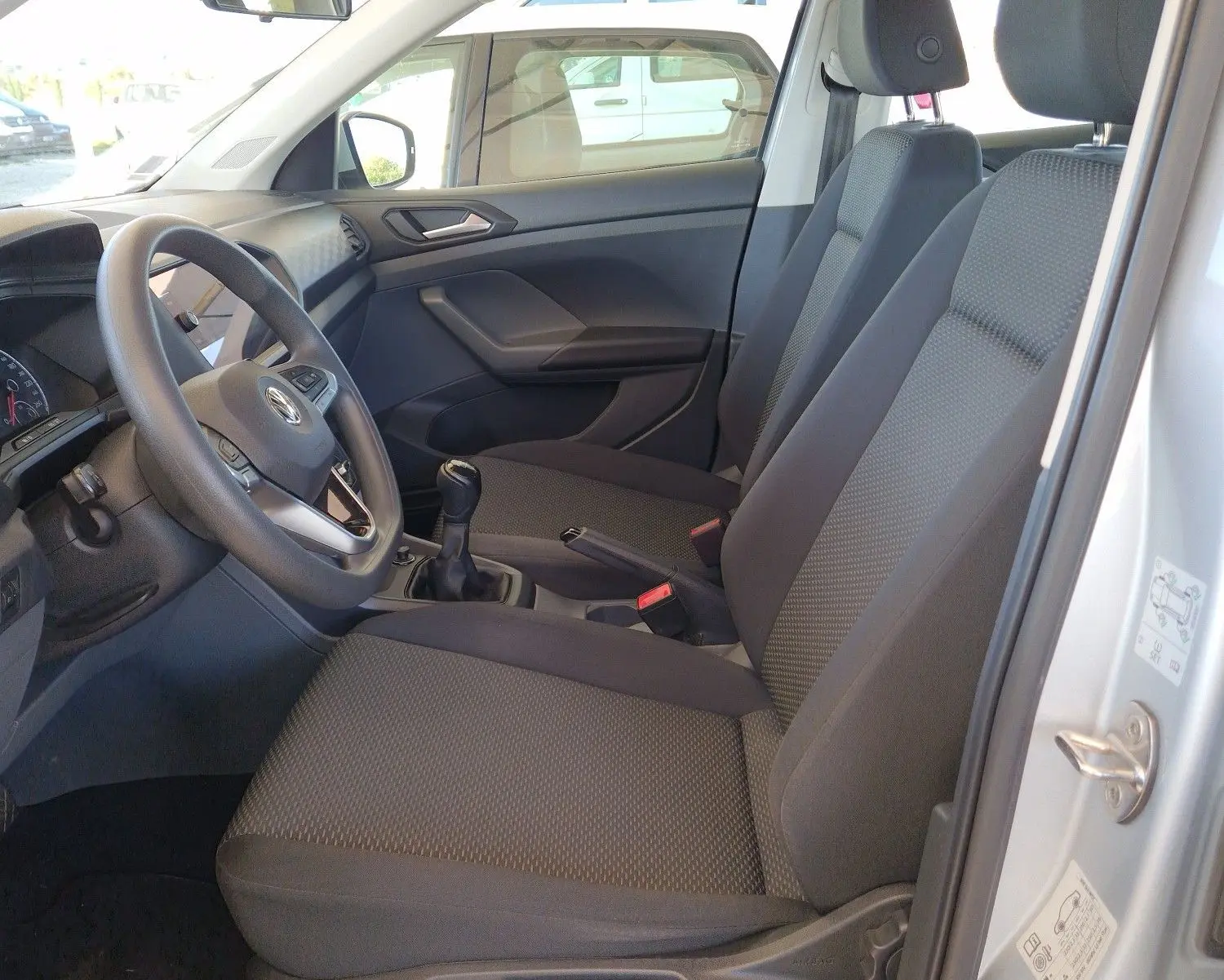 Vue intérieure côté conducteur du Volkswagen T-Cross argent métal 2019, montrant sièges et volant avec boîte manuelle.