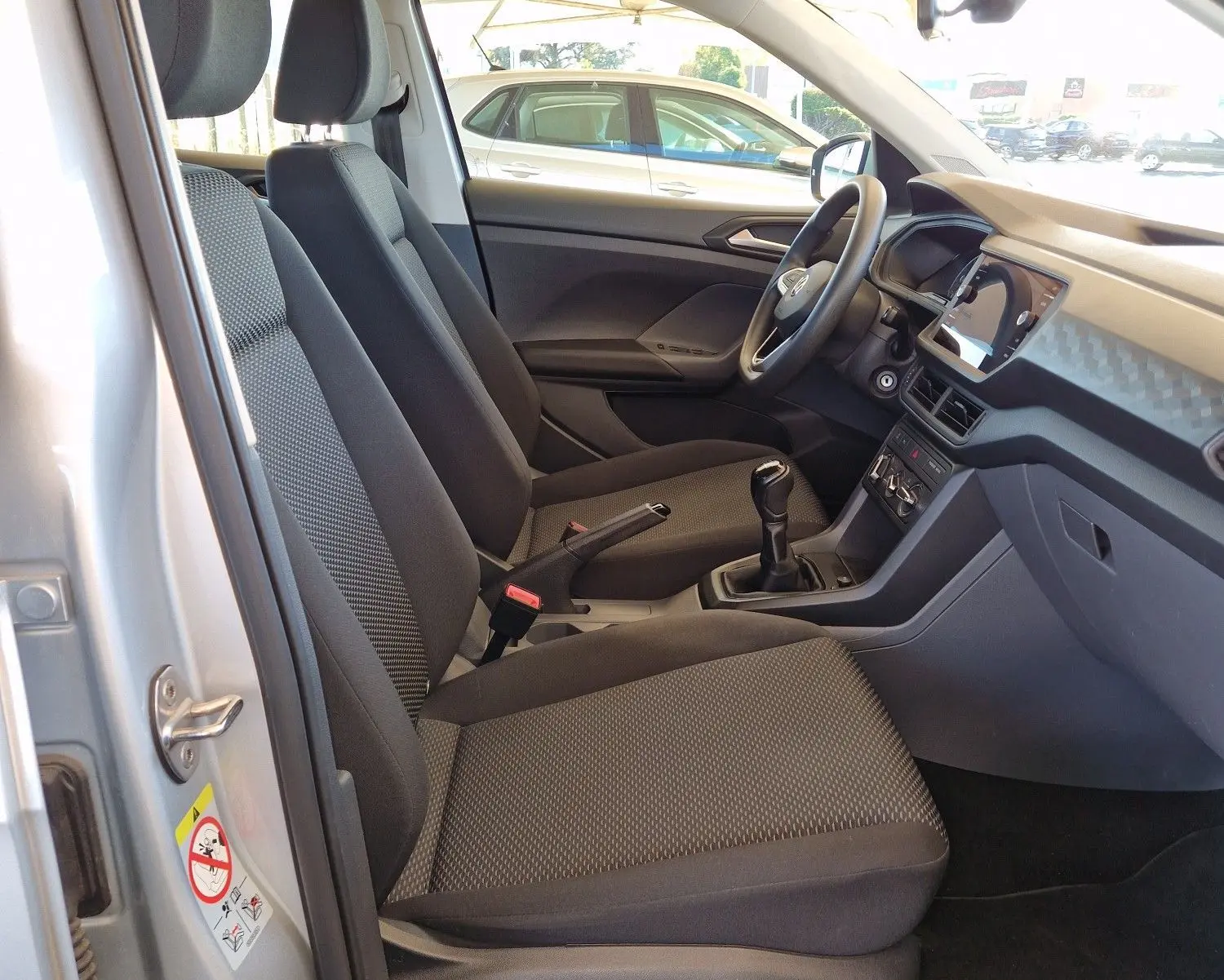 Intérieur côté conducteur du Volkswagen T-Cross argent métal 2019, sièges noirs et tableau de bord moderne avec boîte manuelle.