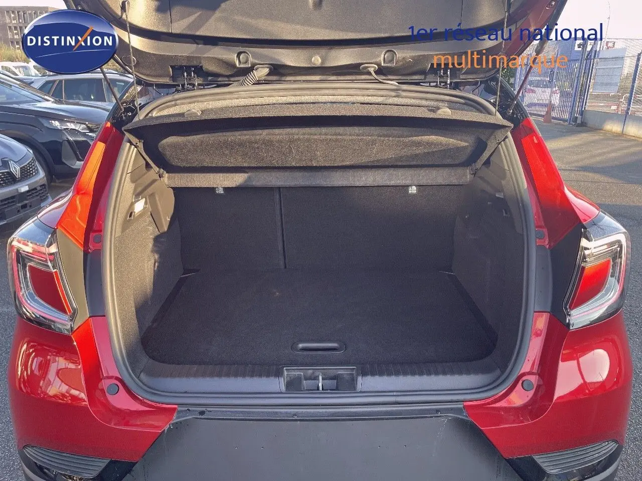 Coffre ouvert vu de l'arrière d'un Renault Captur E-Tech hybride rouge passion avec toit noir, montrant l'espace de chargement vide.