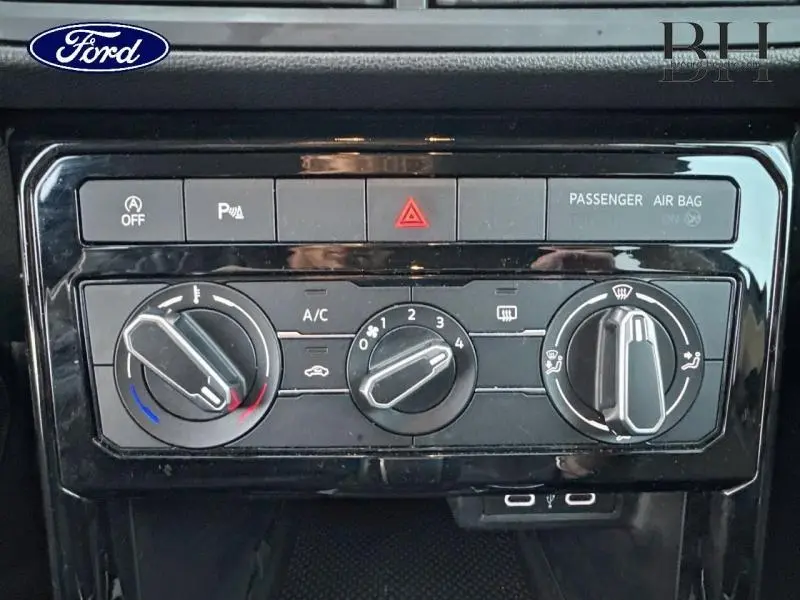 Panneau de commande de climatisation noir brillant du Volkswagen T-Cross 2022, avec boutons rotatifs et indicateurs blancs.