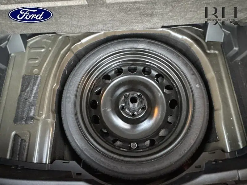 Roue de secours noire vue de dessus dans le coffre d'un véhicule, sans autre élément visible du Volkswagen T-cross.