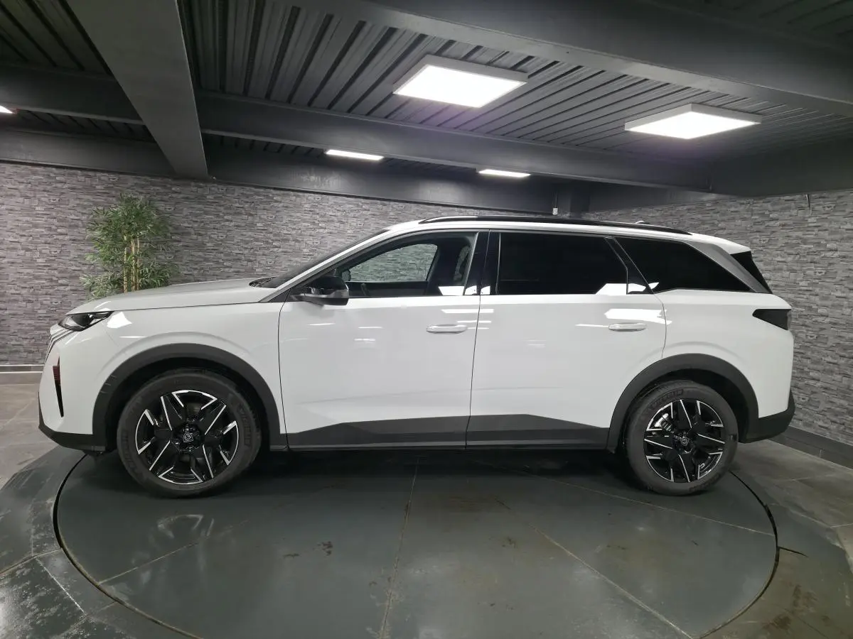 Profil droit du Peugeot 5008 blanc 2025 avec jantes alliage noires et barres de toit noires brillantes.