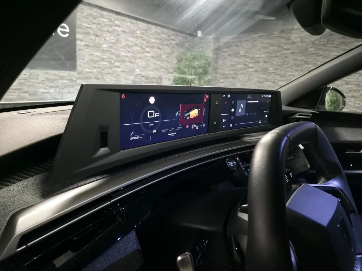 Vue intérieure côté conducteur du tableau de bord numérique et écran tactile du Peugeot 5008 blanc hybride 2025.