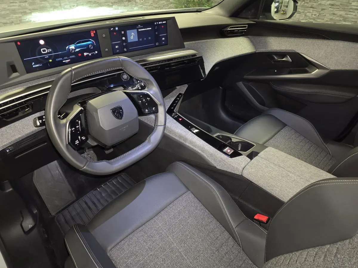 Vue intérieure côté conducteur du Peugeot 5008 2025, avec tableau de bord numérique et sellerie tissu gris et noir.