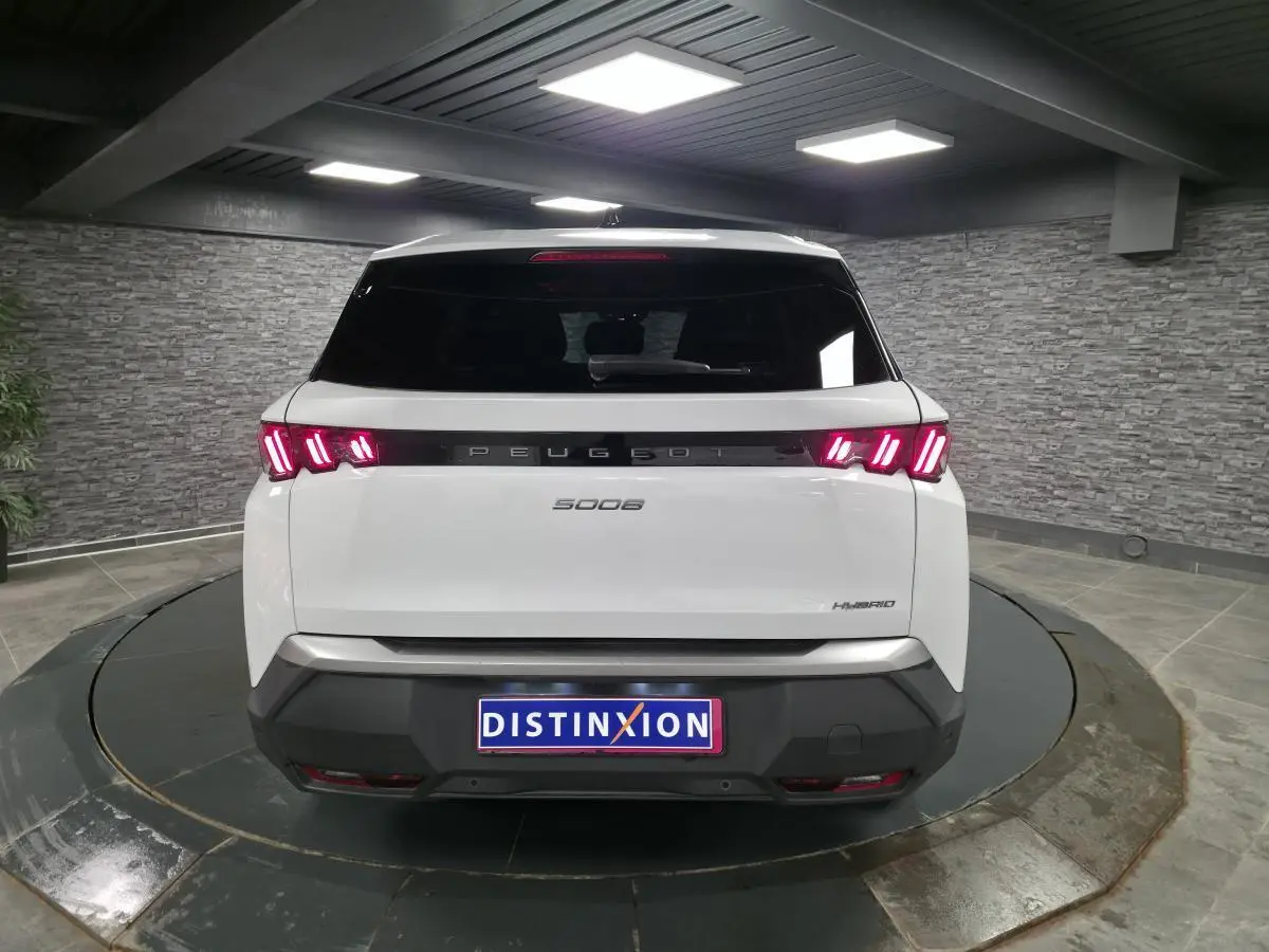 Vue arrière d'un Peugeot 5008 blanc hybride 2025 avec feux arrière LED 3 griffes et bandeau noir laqué.