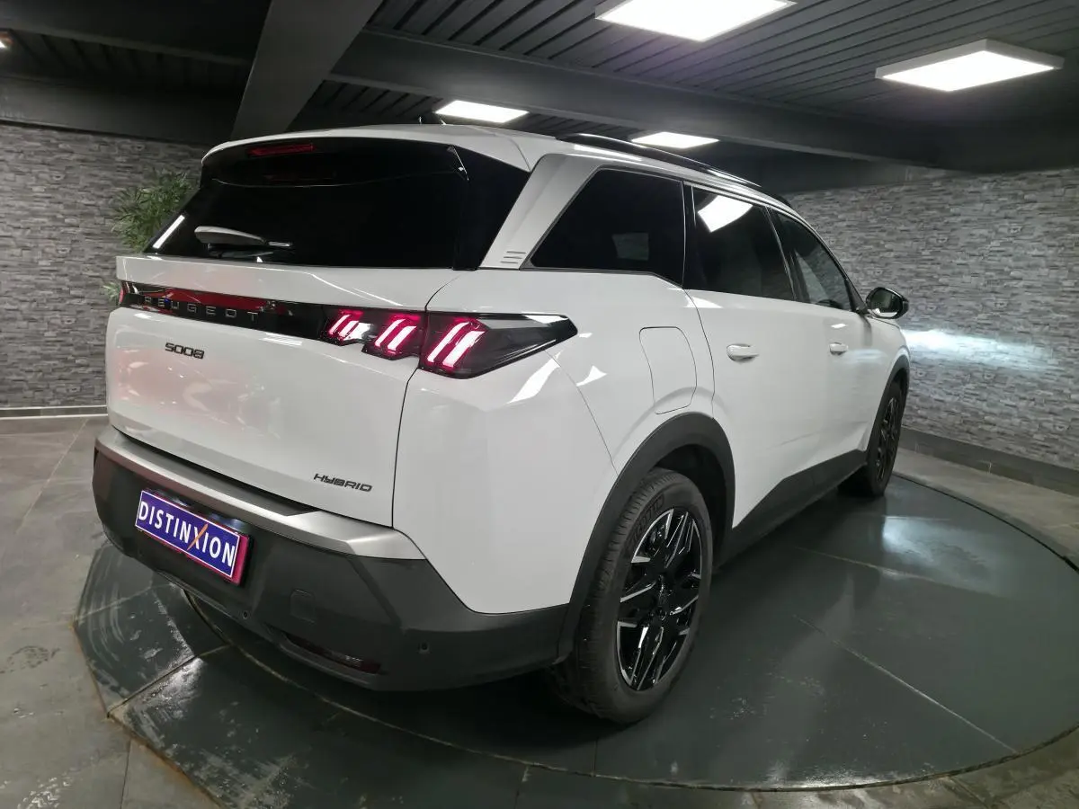 Vue 3/4 arrière droite du Peugeot 5008 hybride blanc avec feux arrière à LED 3 griffes et jantes alliage noires.