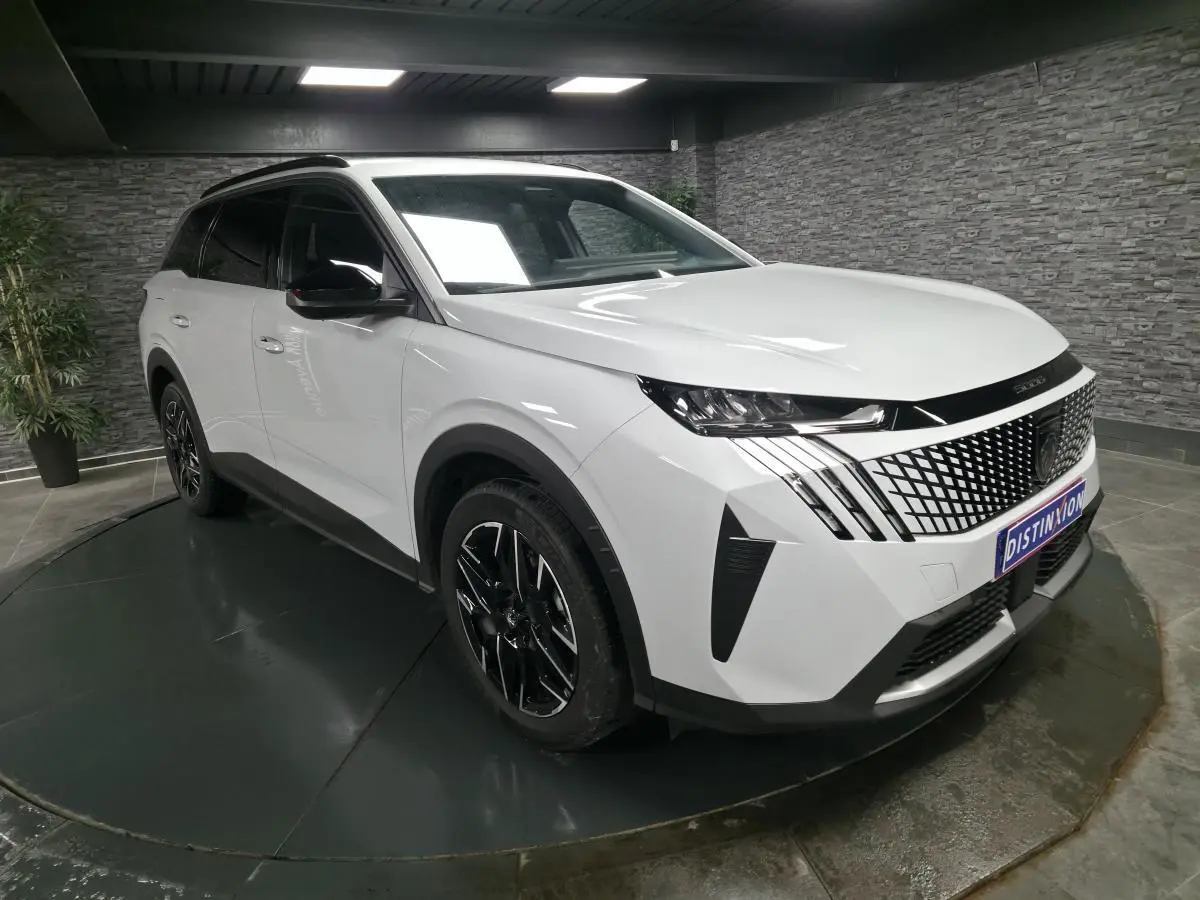 Peugeot 5008 blanc en 3/4 avant droit, avec calandre noire à motif géométrique et jantes alliage noires.