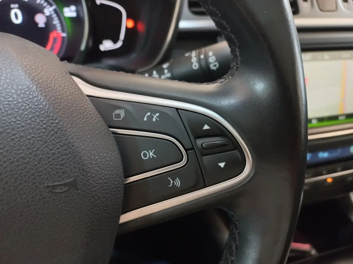 Gros plan sur les commandes multifonctions en cuir du volant du Renault Kadjar Intens Energy TCe 130 EDC, avec écran tactile en arrière-plan.