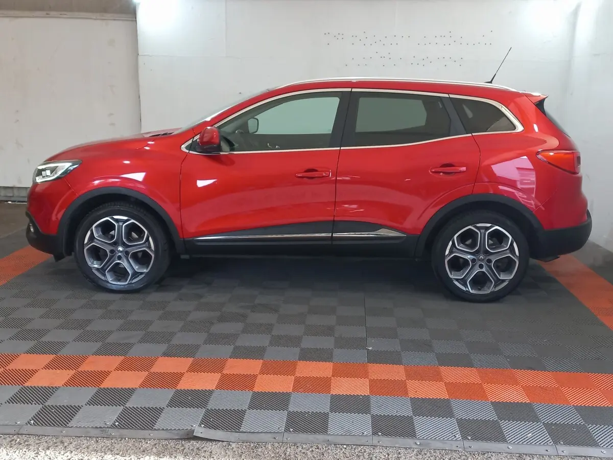 Vue de profil côté gauche d'un Renault Kadjar Intens Energy TCe 130 EDC rouge avec jantes alliage et rails de toit chromés.