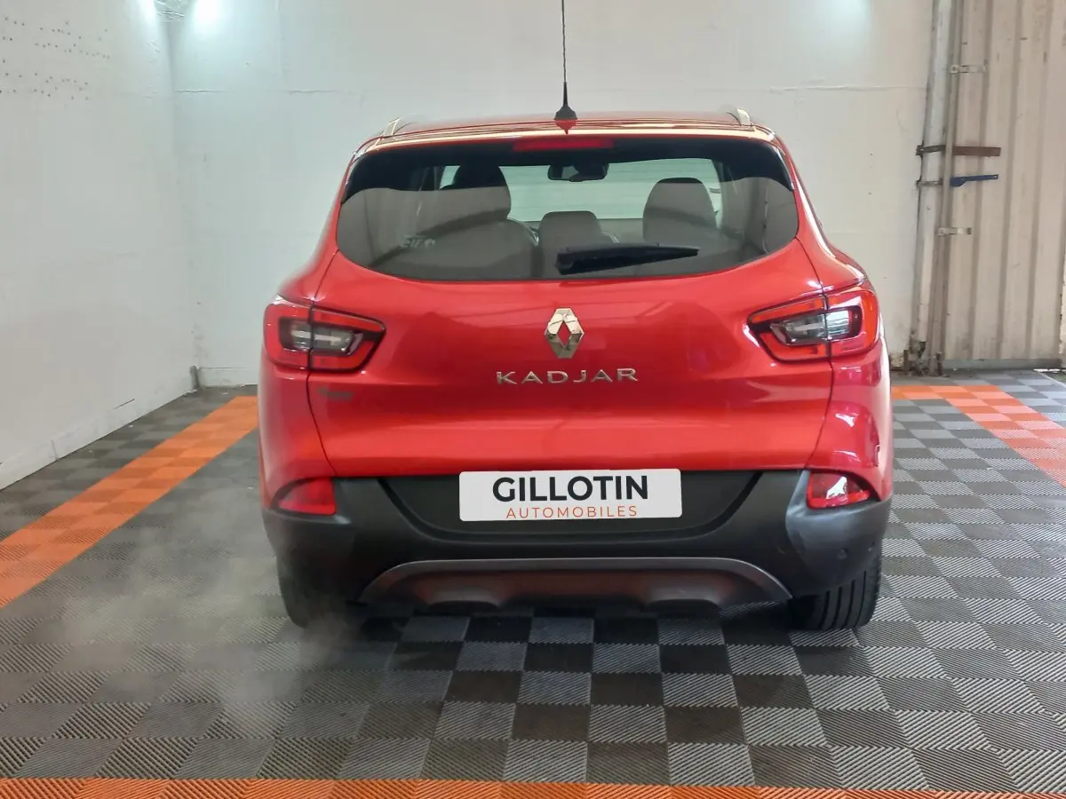 Vue arrière d'un Renault Kadjar rouge avec logo et nom du modèle visibles, dans un garage au sol carrelé noir et orange.