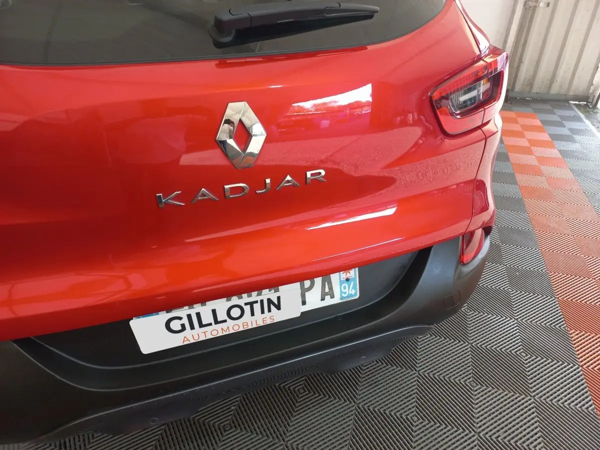 Vue rapprochée arrière d’un Renault Kadjar rouge montrant le logo et le nom du modèle sur un sol à damiers noir et orange.