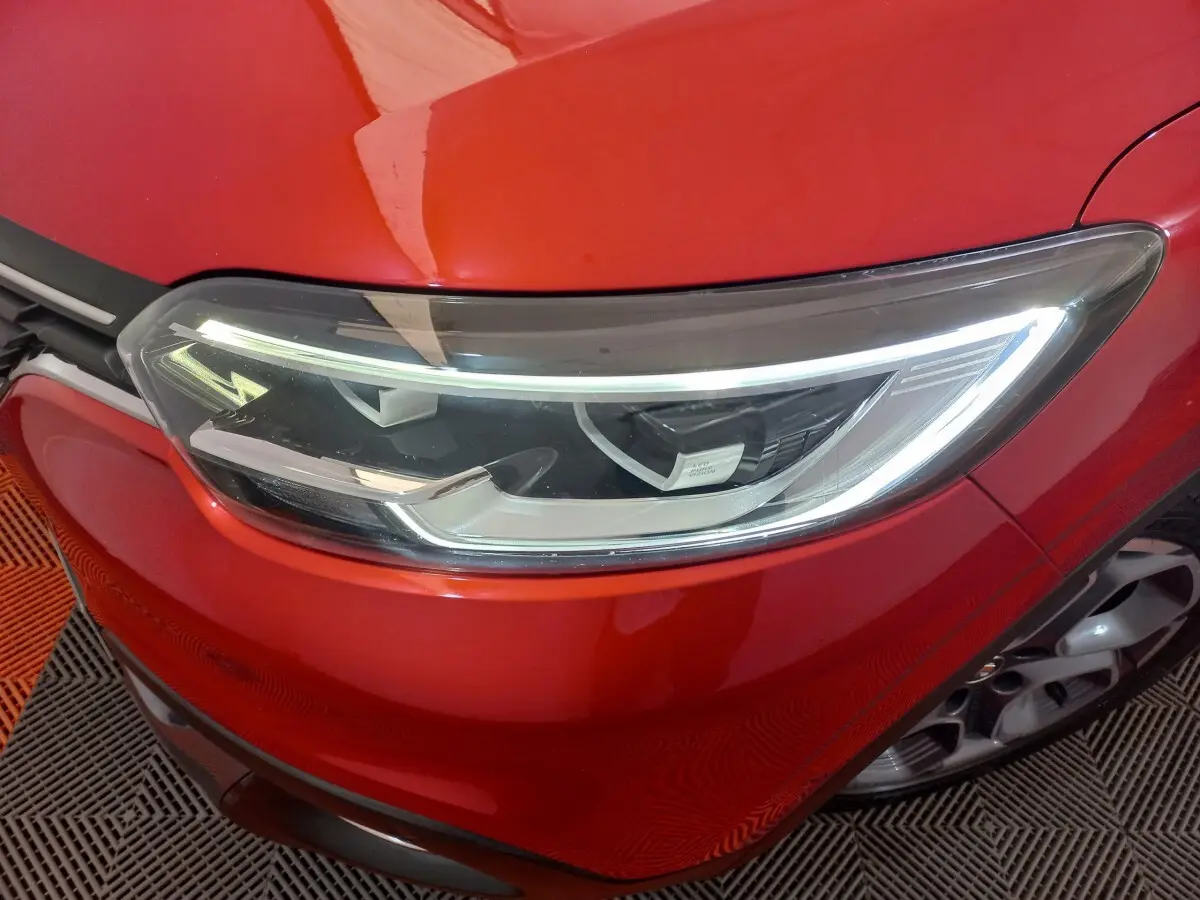 Gros plan sur le phare avant droit du Renault Kadjar rouge, mettant en valeur les feux LED et la calandre chromée.