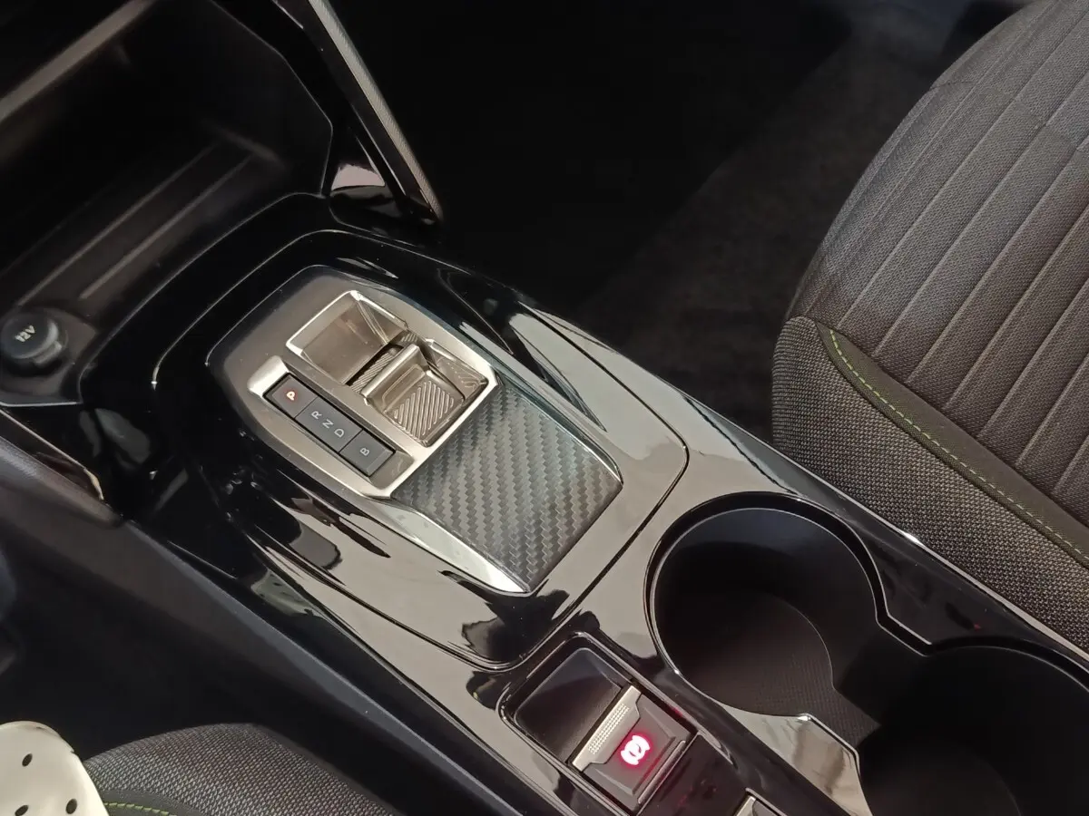 Gros plan sur la console centrale noire brillante avec levier de boîte automatique et frein à main électrique, siège tissu gris à surpiqûres vertes.
