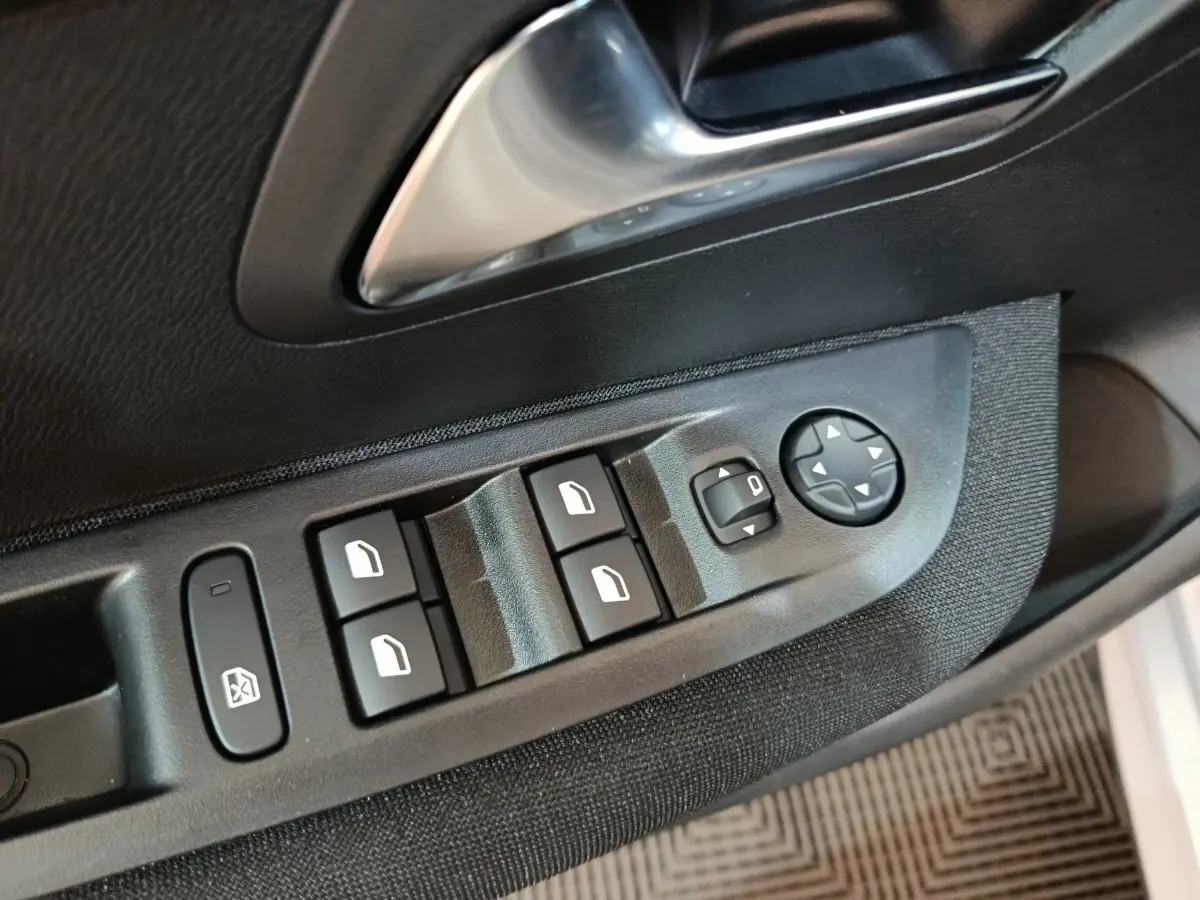 Gros plan sur les commandes de lève-vitres et rétroviseurs côté conducteur d'une Peugeot 208 électrique gris clair.