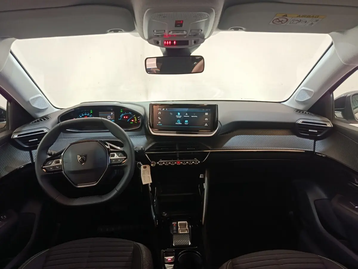 Vue intérieure avant de la Peugeot 208 électrique 2024, tableau de bord noir avec écran tactile central et volant cuir multifonctions.