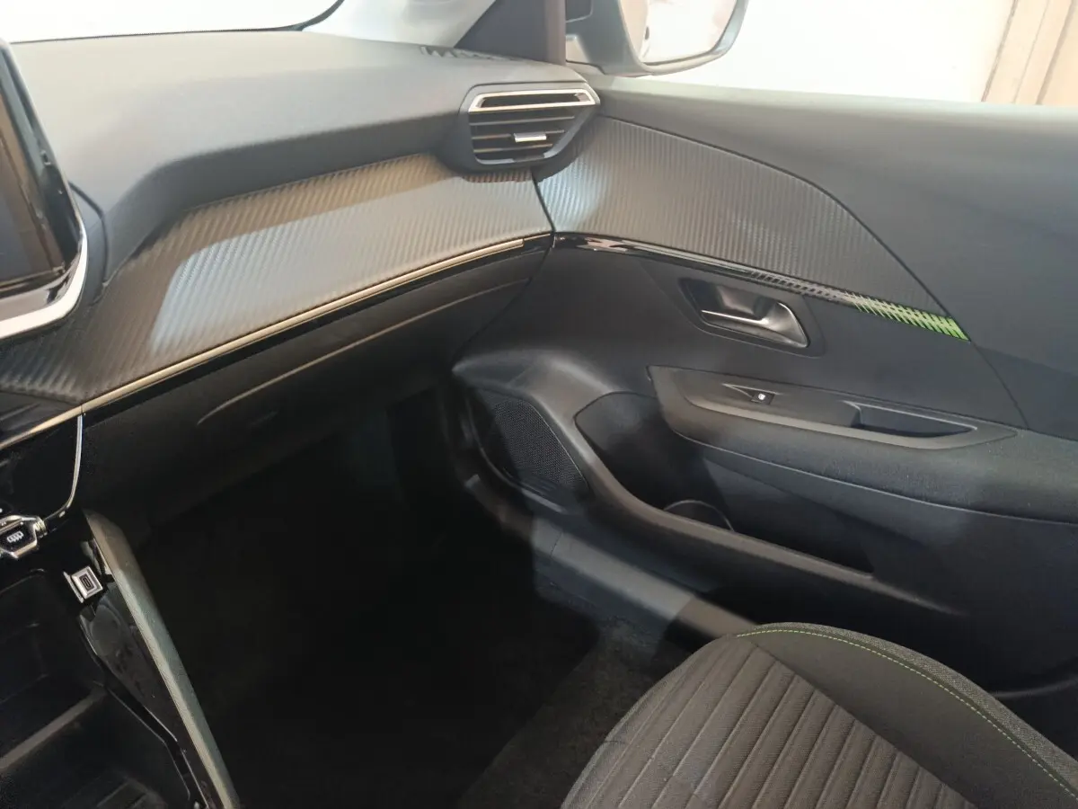 Intérieur côté passager du Peugeot 208 électrique 2024, tableau de bord gris avec finition carbone et siège tissu noir.