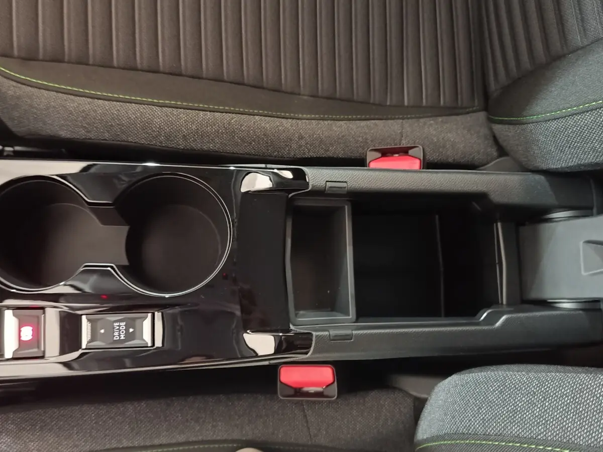 Vue plongeante sur la console centrale noire brillante et les sièges gris avec surpiqûres vertes d'une Peugeot 208 électrique 2024.