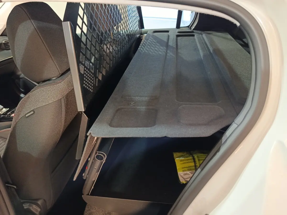 Vue intérieure côté droit du coffre de la Peugeot 208 électrique blanche avec tablette de rangement relevée.