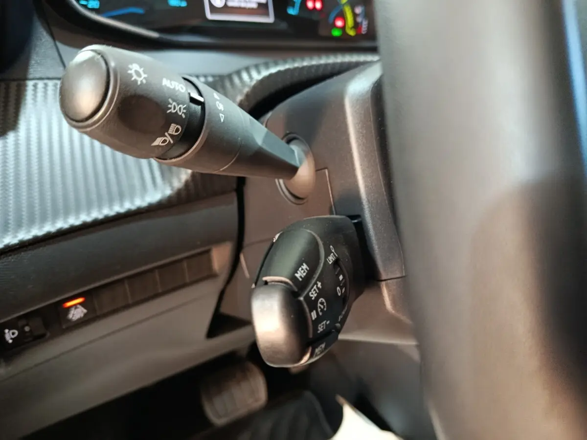 Gros plan sur la commande multifonctions et le commodo d’éclairage du tableau de bord d’une Peugeot 208 électrique blanche.