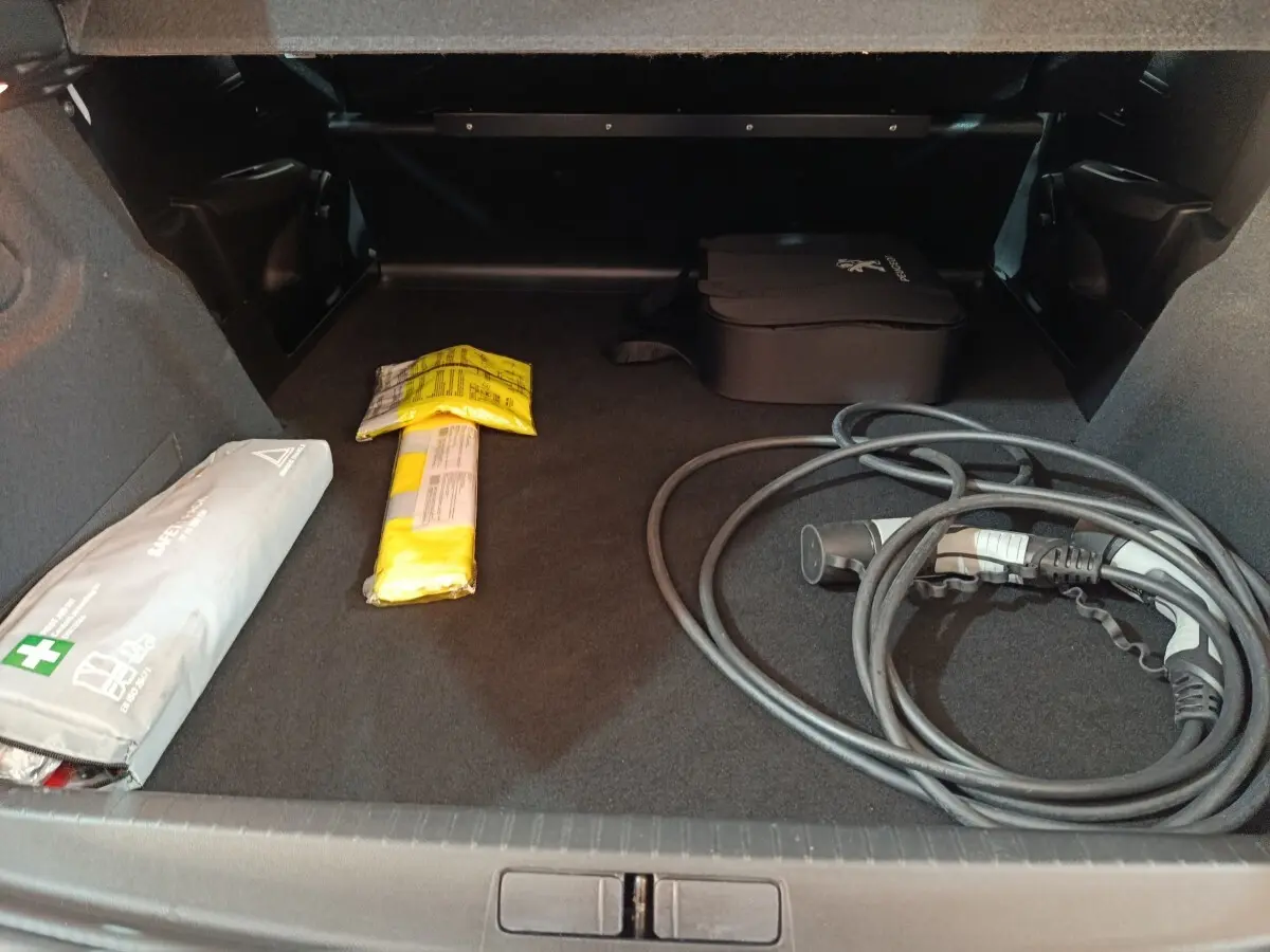 Coffre ouvert vu de face d'une Peugeot 208 électrique blanche de 2020 avec câble de recharge et trousse de secours.