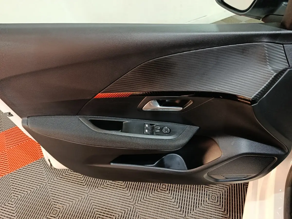 Vue rapprochée de la porte intérieure côté gauche de la Peugeot 208 électrique blanche avec insert décoratif noir et rouge.