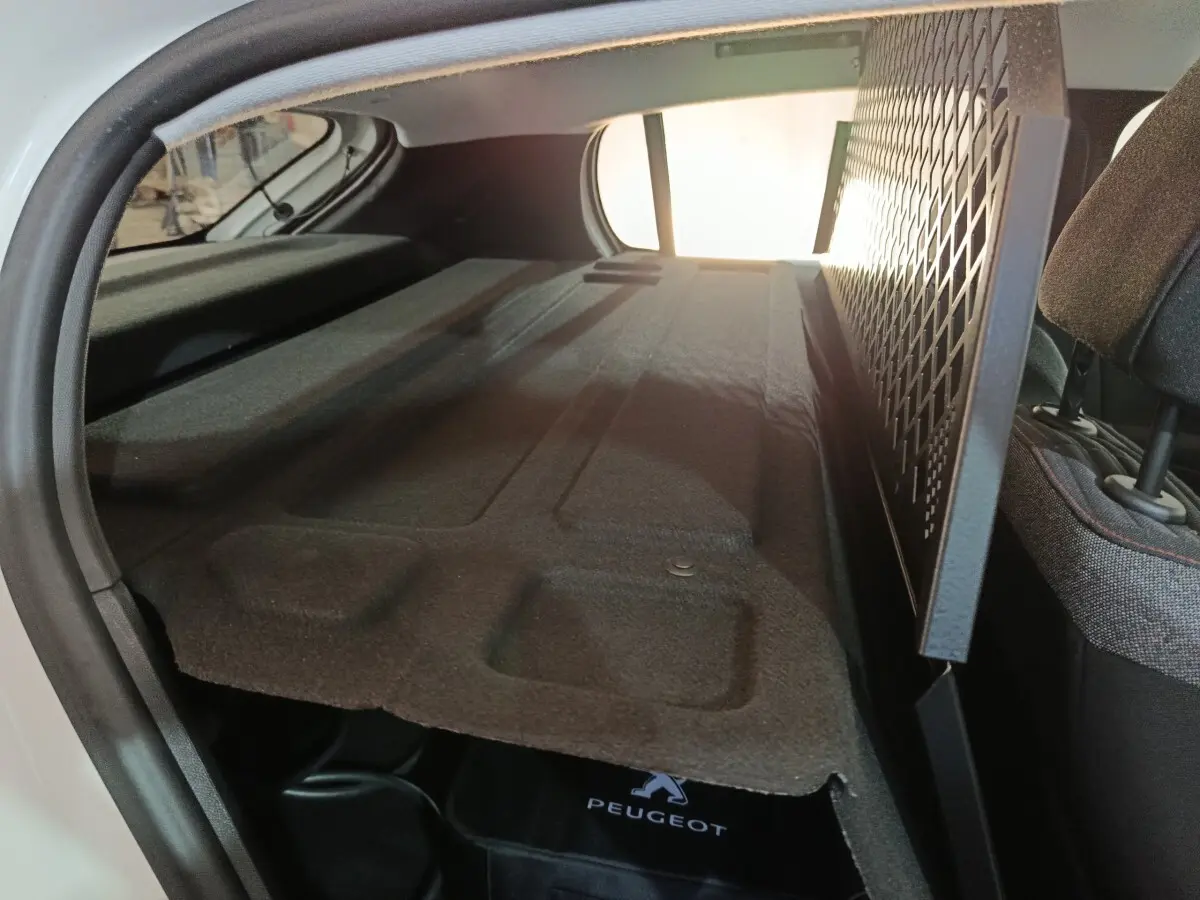 Vue intérieure du coffre arrière d'une Peugeot 208 électrique blanche, avec séparation grillagée et banquette rabattue.