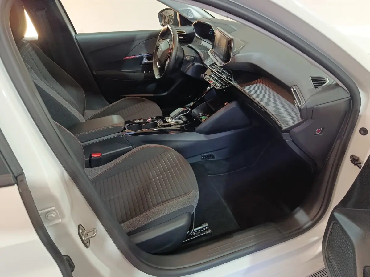 Vue intérieure côté conducteur de la Peugeot 208 électrique blanche, avec volant cuir multifonctions et tableau de bord digital.